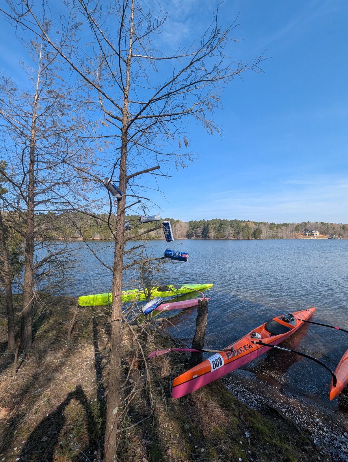 Outrigger canoes resting at the Hyco Lake shoreline beneath blue sky and bare winter trees.